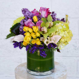 Mixed bouquet of roses, orchids, and hydrangeas in a green glass vase
