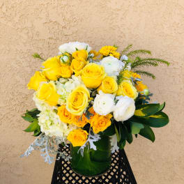 Yellow and white rose bouquet in a green glass vase
