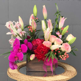 Mixed bouquet with pink lilies, roses, orchids, and red blooms in a wooden box