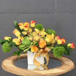 Yellow and orange roses with green accents in a white vase