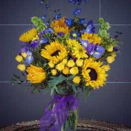 Bouquet of yellow sunflowers and blue flowers in a glass vase with a purple ribbon