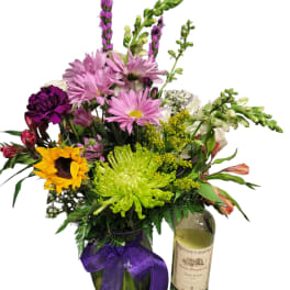 Mixed bouquet in a glass vase beside a wine bottle