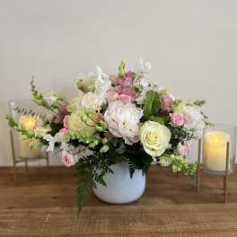 Pink and white floral arrangement in a white vase with candles beside it