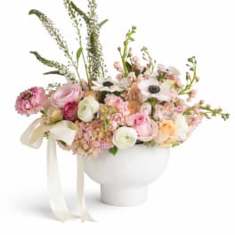 Pastel floral arrangement in a white pedestal vase with ribbon
