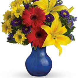 Colorful bouquet of lilies, gerbera daisies, and purple filler in a blue vase