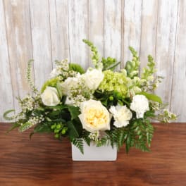 Low arrangement of white and pale yellow roses and carnations in a white rectangular vase
