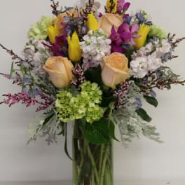 Mixed bouquet of roses, tulips, and purple orchids in a glass vase