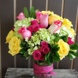 Vase arrangement of yellow and pink roses with green hydrangeas in a clear glass vase
