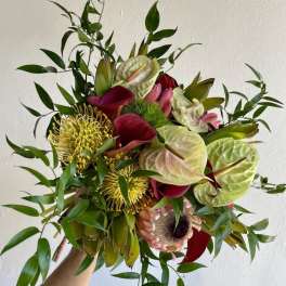 Tropical bouquet with red anthuriums, yellow pincushion blooms, and greenery