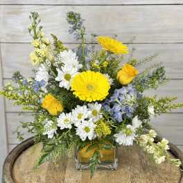 Mixed bouquet of yellow, white, and blue flowers in a glass vase
