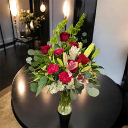 Bouquet of red roses, pink lilies, and white blooms in a glass vase