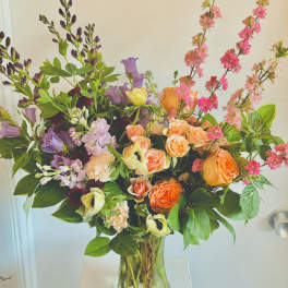 Mixed bouquet of orange, pink, and purple flowers in a clear glass vase
