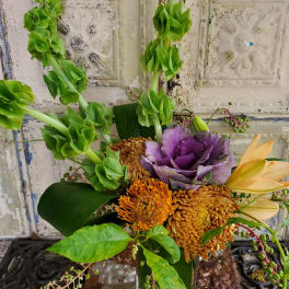 Bouquet with green bells of Ireland, purple cabbage, and orange blooms in a vase