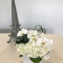 White orchids and hydrangeas in a white box beside a small Eiffel Tower decoration