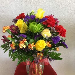 Colorful mixed bouquet with roses, carnations, and purple filler in a glass vase