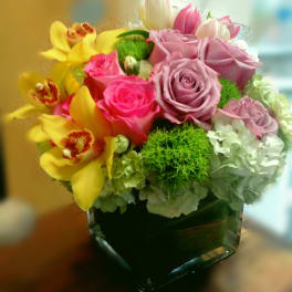 Bouquet of pink roses and yellow orchids in a square glass vase