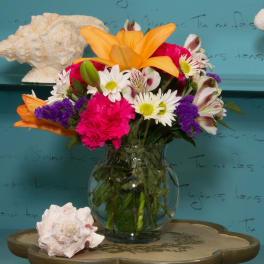 Colorful mixed bouquet in a clear glass vase with orange lilies and daisies