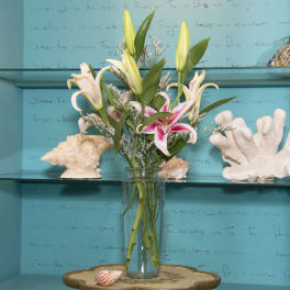 Pink and white lilies arranged in a clear glass vase