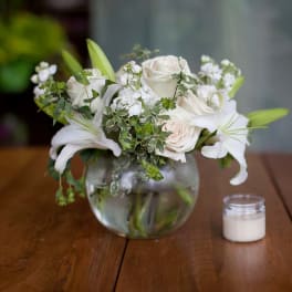 White roses and lilies arranged in a round glass vase