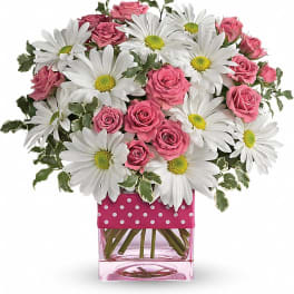 Pink roses and white daisies in a square glass vase with a polka-dot ribbon