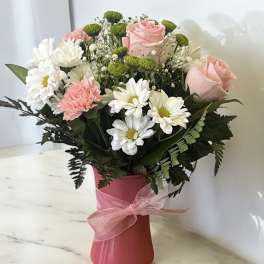 Pink roses and white daisies in a pink vase with a ribbon