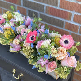 Long wooden box arrangement with pink gerbera daisies, roses, dahlias, blue hyacinths, and yellow protea.