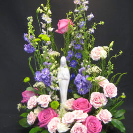 Tall floral arrangement with pink and purple roses around a white statue
