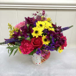 Bright mixed flower arrangement in a colorful patterned mug-style container