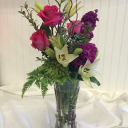 Tall bouquet of pink roses, white lilies, and purple flowers in a glass vase