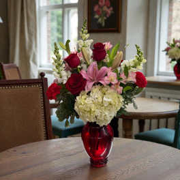 Mixed pink and red flowers in a red glass vase on a table