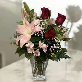 Bouquet of pink lilies and red roses in a clear glass vase