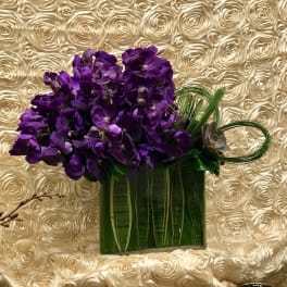 Purple orchid arrangement in a green rectangular vase