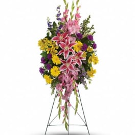 Standing floral spray with pink lilies, yellow daisies, and purple flowers on an easel
