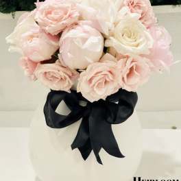 Blush pink and white roses in a white vase with a black ribbon