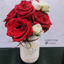 Red and white roses in a white mason jar vase