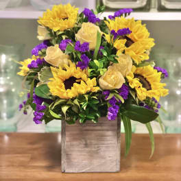 Yellow sunflowers, cream roses, and purple filler flowers in a wooden box