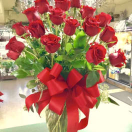 Tall bouquet of red roses in a glass vase with a large red ribbon