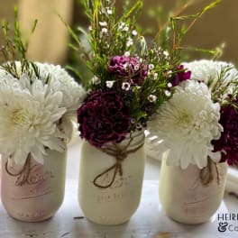Three mason jars holding white and burgundy flowers