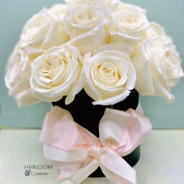 White roses arranged in a black vase with a pale pink ribbon