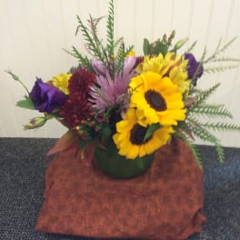 Mixed bouquet with sunflowers, purple blooms, and red flowers in a green vase