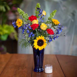 Sunflowers, yellow roses, red carnations, and blue flowers in a tall vase