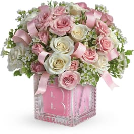 Pink and white roses arranged in a clear glass cube vase with pink ribbons