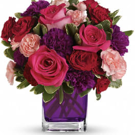 Pink and red roses with purple carnations in a purple glass vase