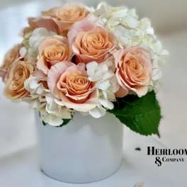 Peach roses and white hydrangeas in a white hatbox