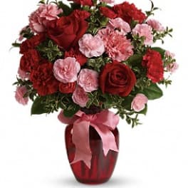 Red roses and pink carnations in a red vase with a pink ribbon