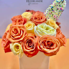 Orange and cream roses in a white square vase with a sprinkle-covered treat