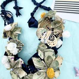 Money lei with ribbon and paper flowers beside a graduation card
