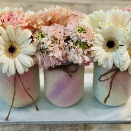 Three pastel mason jars with daisy and pink flower arrangements