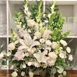 White floral arrangement with lilies, roses, and snapdragons in a low container