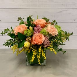 Peach roses and mixed blooms arranged in a square glass vase